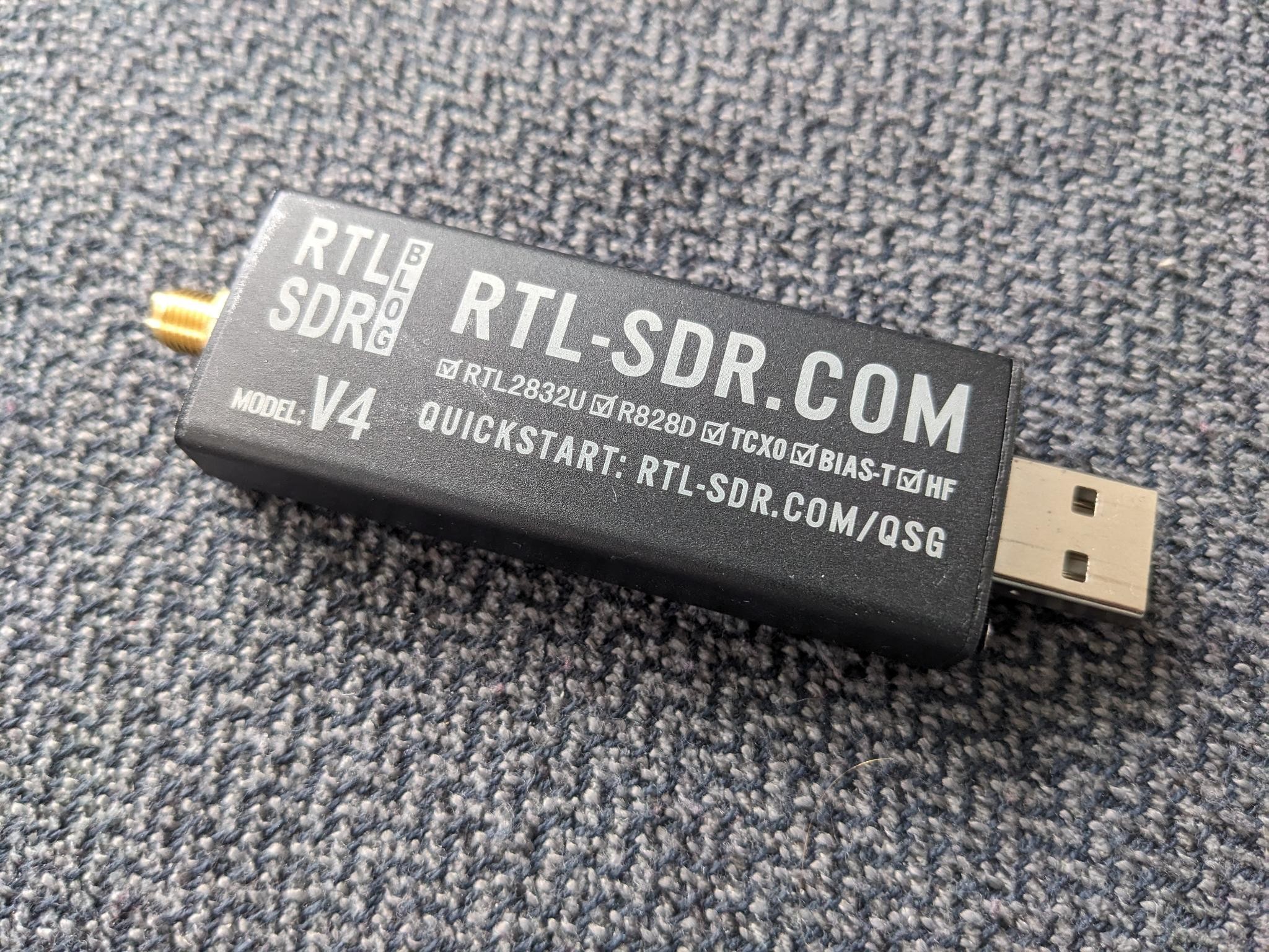 The device looks like a big USB stick with a bronze screw connector at the back end. It's labelled "RTL-SDR Blog V4".